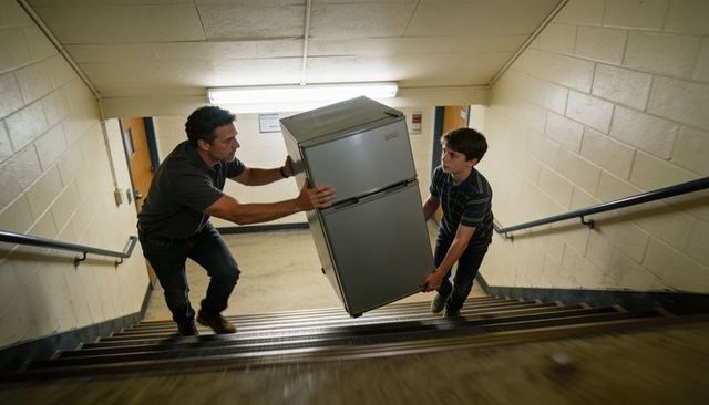 Man and teen carrying refrigerator up narrow stairwell