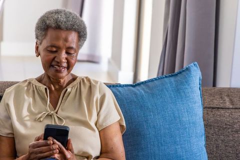 Senior african american woman relaxing on sofa using smartphone with blue throw pillow