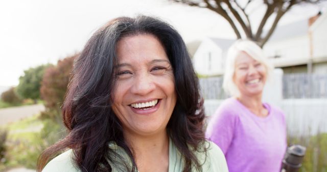 Two older women are smiling and enjoying an outdoor activity in a suburban neighborhood. The scene conveys happiness, friendship, and healthy living. Good for advertisements and articles about friendship, healthy senior lifestyles, outdoor activities, and active retirement living.