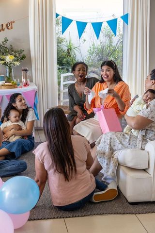 Diverse friends celebrating baby shower with gift unwrapping