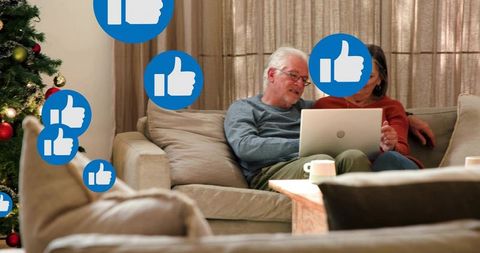 Senior couple sharing laptop on cozy sofa celebrating christmas with floating like icons