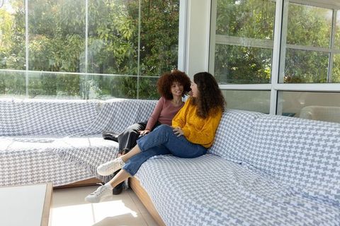 Women chatting on sunroom sofa with houndstooth throw, casual conversation in sunlit room
