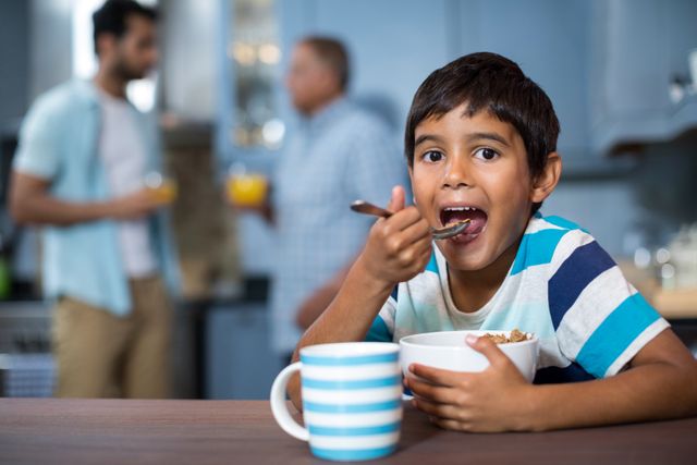 Portrait of boy having cereal breakfast with family in background at home