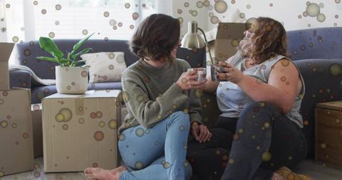 Sipping mugs while unpacking boxes sitting on living room floor cozy friendship moment