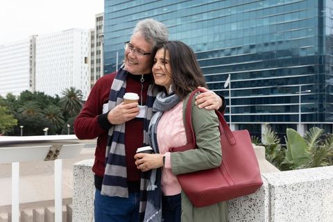 Mature couple enjoying coffee on urban balcony, smiling and embracing against skyline