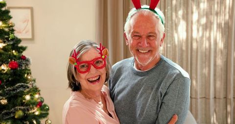 Senior Couple Embracing in Festive Antlers by Christmas Tree