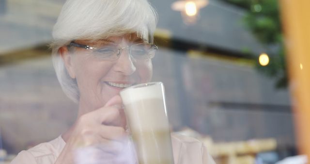Senior Caucasian woman enjoys a latte at a cozy cafe. Her smile suggests a moment of relaxation during a pleasant coffee break.