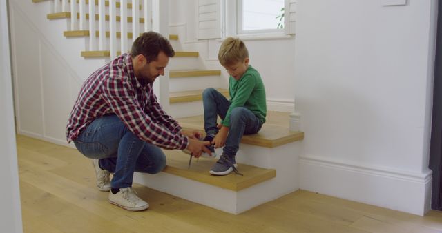 Happy caucasian father with son tying his shoes on stairs at home. Domestic life, family and lifestyle, unaltered.