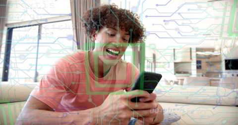 Young man smiling while using smartphone on couch with circuit board digital overlay