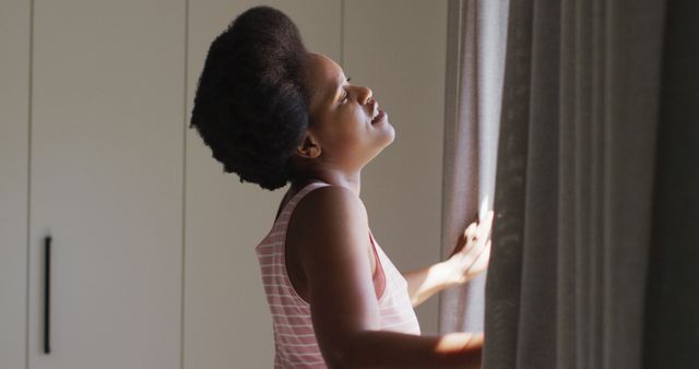 Happy african american woman widening curtains in bedroom. domestic lifestyle, spending free time at home.