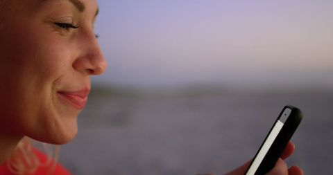 Young Woman Smiling While Using Smartphone at Dusk on Beach - Download Free Stock Images Pikwizard.com