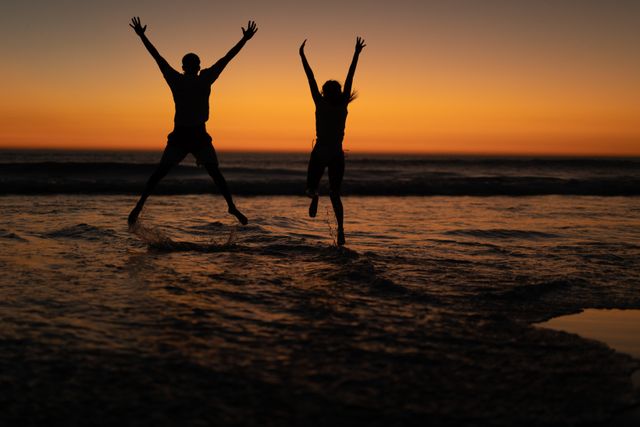 Silhouette of couple jumping together with arms up on the beach