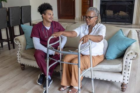African american senior woman using walker at home with friendly caregiver assisting