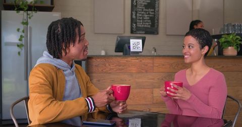 Couple chatting over coffee holding red mugs in cozy cafe