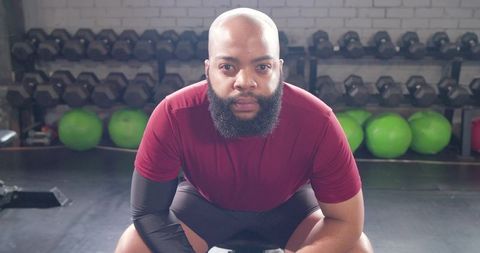 Focused athlete crouching on bench preparing for heavy lift in gym with free weights