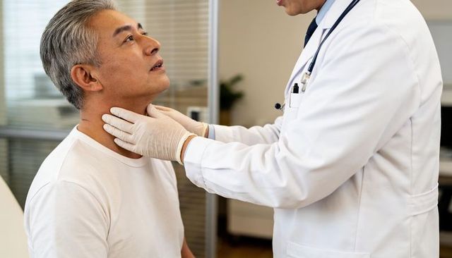 Physician palpating senior patient neck during routine medical examination with gloves