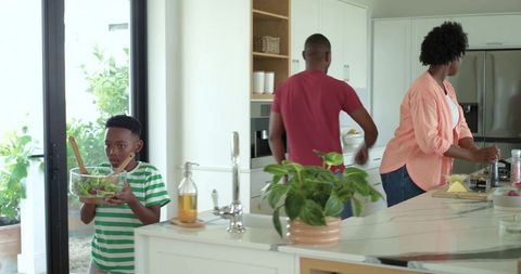 African american family preparing meal in bright modern kitchen with child stirring salad