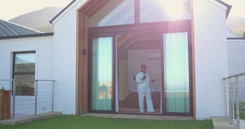 Mid-adult african american woman standing in sunlit doorway holding mug and smartphone