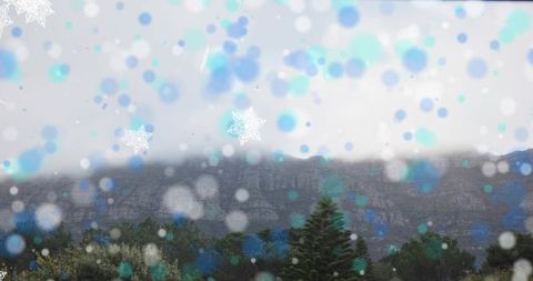 Snowflakes drifting over misty mountain ridge with evergreen treeline and bokeh lights