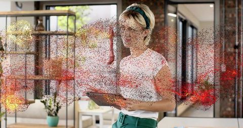 Woman holding tablet viewing holographic data cloud particles in sunlit open-plan studio