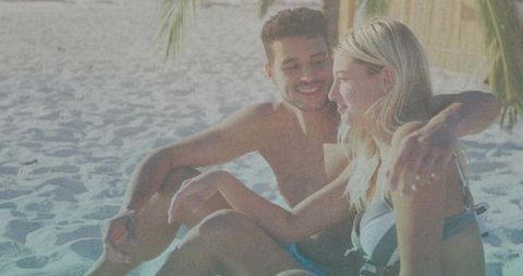 Sunlit couple cuddling on tropical beach beneath palm fronds, relaxed vacation romance