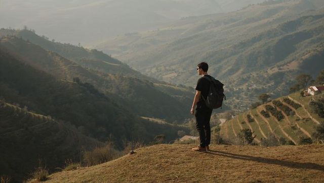 Solo hiker standing on ridge overlooking sunlit terraced valley during golden hour