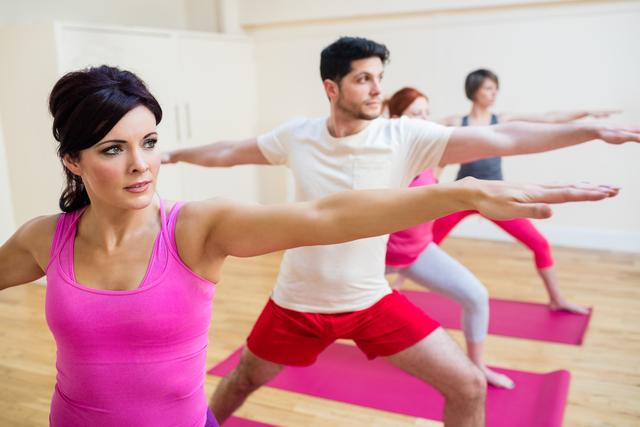 This image depicts a group of people engaged in a yoga class, performing stretching exercises on yoga mats in a well-lit fitness studio. Ideal for use in content promoting fitness classes, wellness programs, healthy lifestyle tips, and physical activity advertisements.