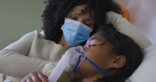 Mother supporting her sick child in hospital with oxygen mask. The mother wears a protective face mask, emphasizing safety and care. Ideal for use in medical, healthcare, and family-oriented contexts, or articles and advertisements focusing on patient care, family support, and the emotional aspects of recovery.