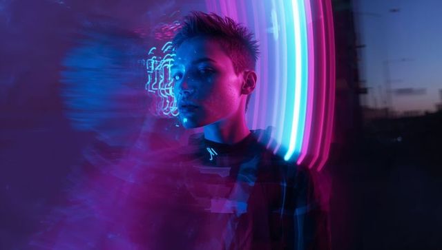Posing young male-presenting model on neon rooftop, creating moody futuristic portrait