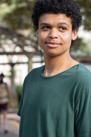 African american young man standing in sunlit park wearing green t-shirt, looking away
