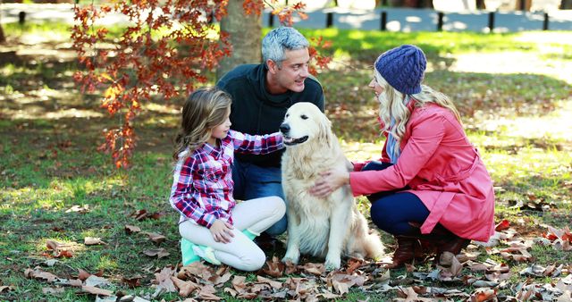 Happy family spending time with their golden retriever in a park during autumn. They are enjoying the outdoors surrounded by fallen leaves. This can be used for advertisements, websites, or articles relating to family bonding, outdoor activities, pet lovers, or autumn scenery.