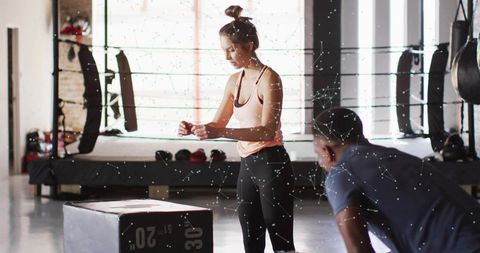 Woman wrapping wrist wraps before plyo box workout in industrial boxing gym with trainer