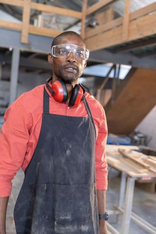 African american woodworker wearing safety goggles and ear protection in workshop