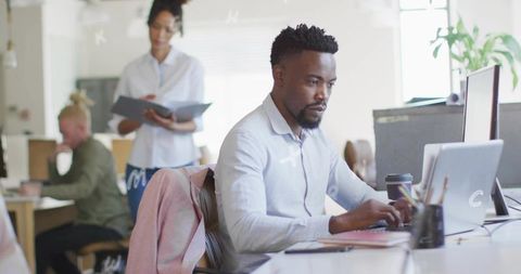 Mid-career professional typing on laptop in modern open-plan office with collaborative team