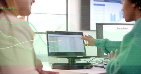 Two women collaborating over data dashboards pointing at quarterly report on monitor