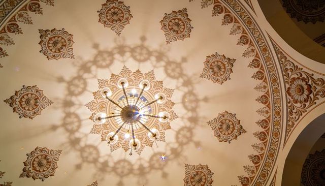 Brass chandelier casting ornate shadow across gilded domed ceiling with medallions