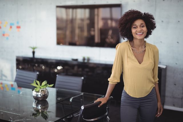 This image depicts a confident businesswoman smiling in a modern meeting room. Ideal for use in corporate websites, business presentations, career development materials, and professional networking platforms to convey themes of leadership, success, and a positive work environment.