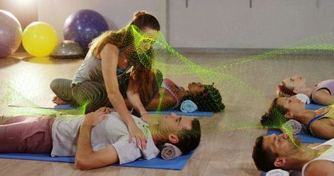 Kneeling instructor teaching cpr while placing hands on participant chest in group fitness class