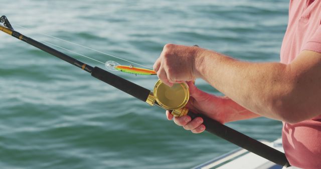 Person preparing fishing rod by attaching lure while on boat in sunny weather, ideal for representing outdoor activities, hobbies, and angling trips. Perfect for articles on fishing techniques, leisure activities, and experiences on the water.