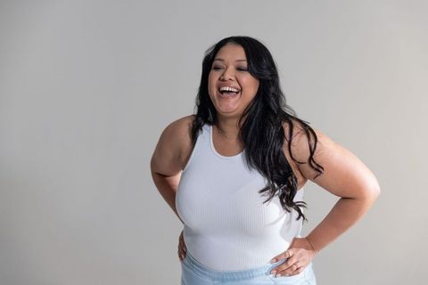 Laughing plus-size woman wearing white ribbed top and denim, joyful casual lifestyle portrait
