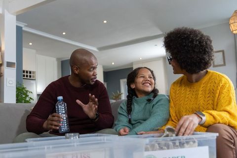 Diverse family organizing recycling with labeled bins on sofa, smiling and sorting