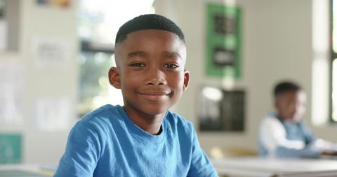 African american boy smiling while sitting at classroom desk holding notebook and learning