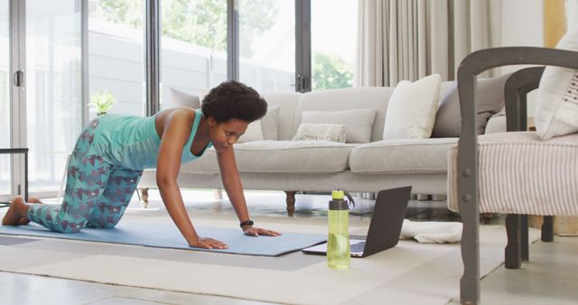 Happy african american wearing sportswear, exercising, using laptop. domestic lifestyle, spending free time at home.
