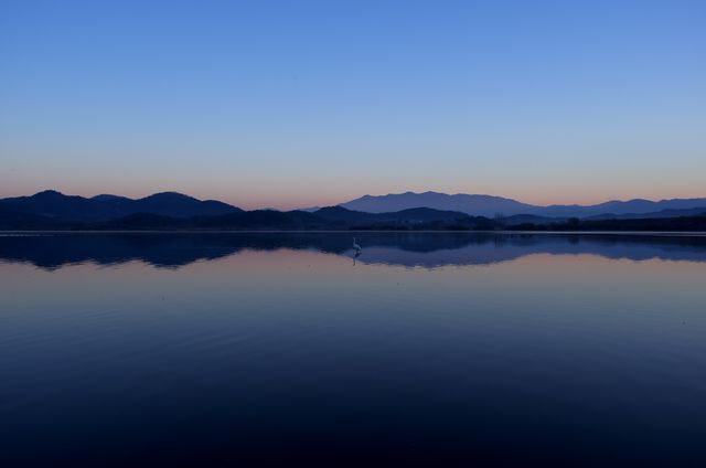 Serene sunset over a tranquil lake reflecting majestic mountains and clear sky, capturing calmness and beauty. Great for background imagery, travel brochures, nature photography collections, and inspirational quotes.