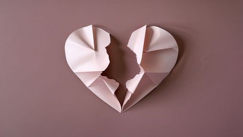 Torn pastel pink paper heart represents heartbreak concept