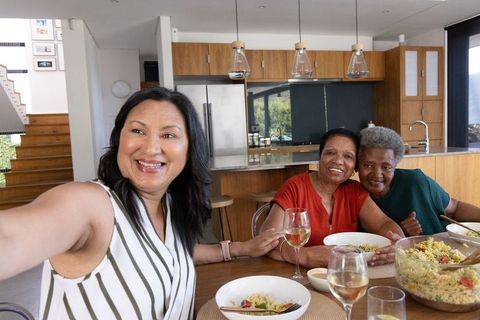 Multigenerational african american women taking selfie sharing pasta and wine in modern kitchen