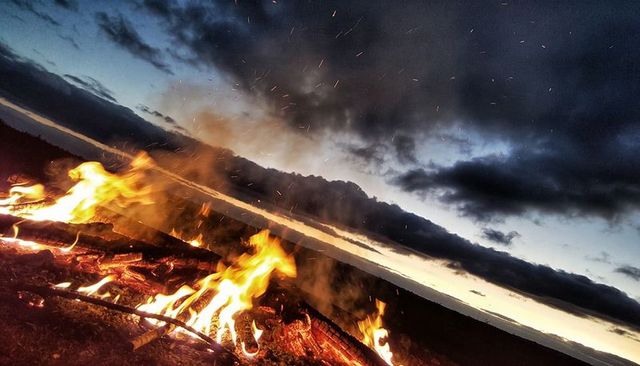 Glowing campfire burning on hillside at dusk with embers flying into dramatic sky