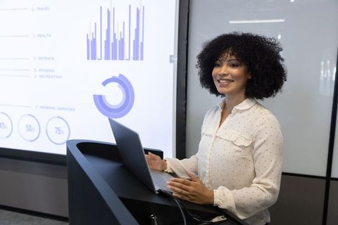 Confident Female Presenter Displaying Charts in Modern Corporate Environment
