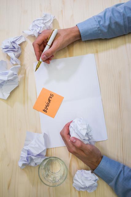Hands of business executive holding crumpled paper and pen on a desk