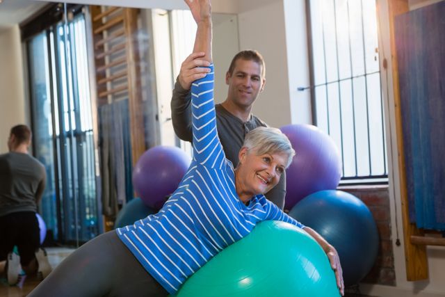 Senior woman engaged in a physiotherapy session with a physiotherapist, using a fitness ball for exercises. Image can be used for healthcare, rehabilitation, and senior fitness promotions.